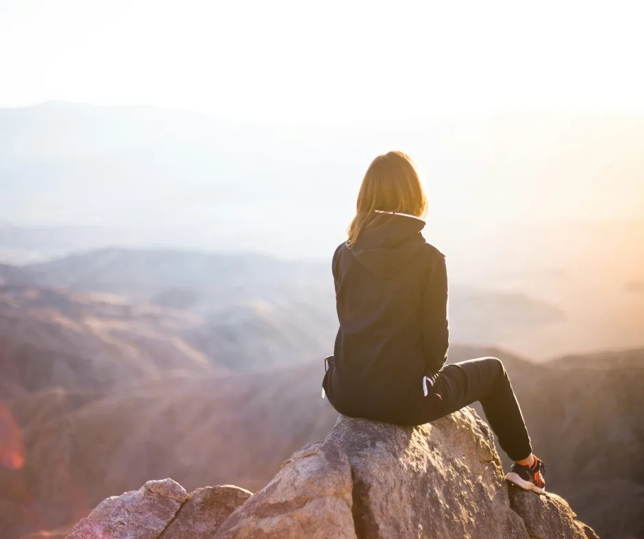 Woman sitting on a rock up a mountain looking at the serene view